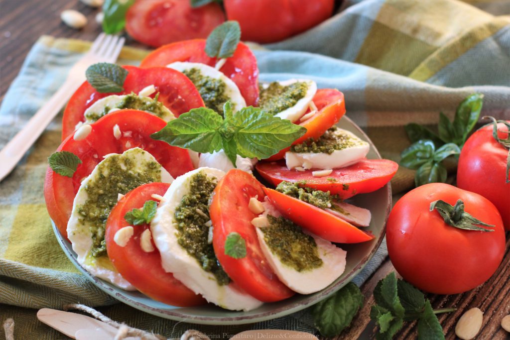 La caprese con pesto di basilico e menta alle mandorle è una gustosa variante del noto piatto a base di pomodoro e mozzarella; una ricetta che non manca mai sulla tavola estiva! Pochi semplici passaggi per un piatto buono e gustoso, ricco di sali minerali e proteine.